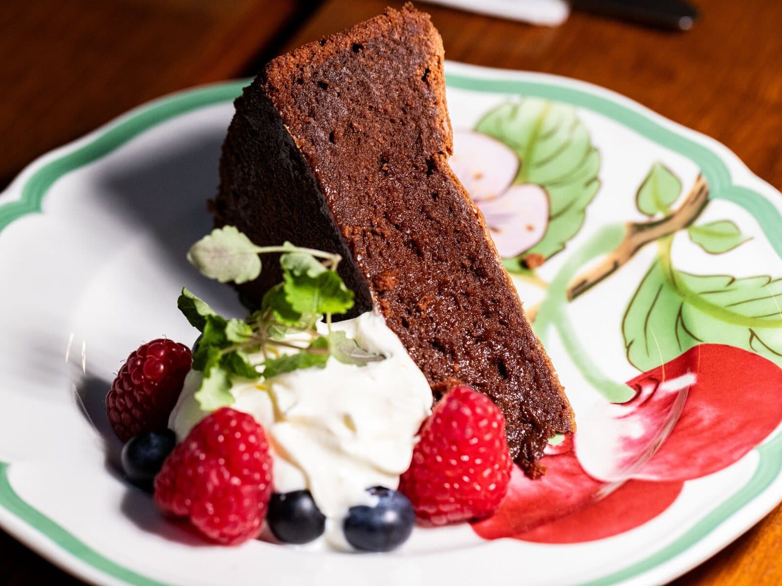 A dense slice of dark chocolate cake with whipped cream and berries.