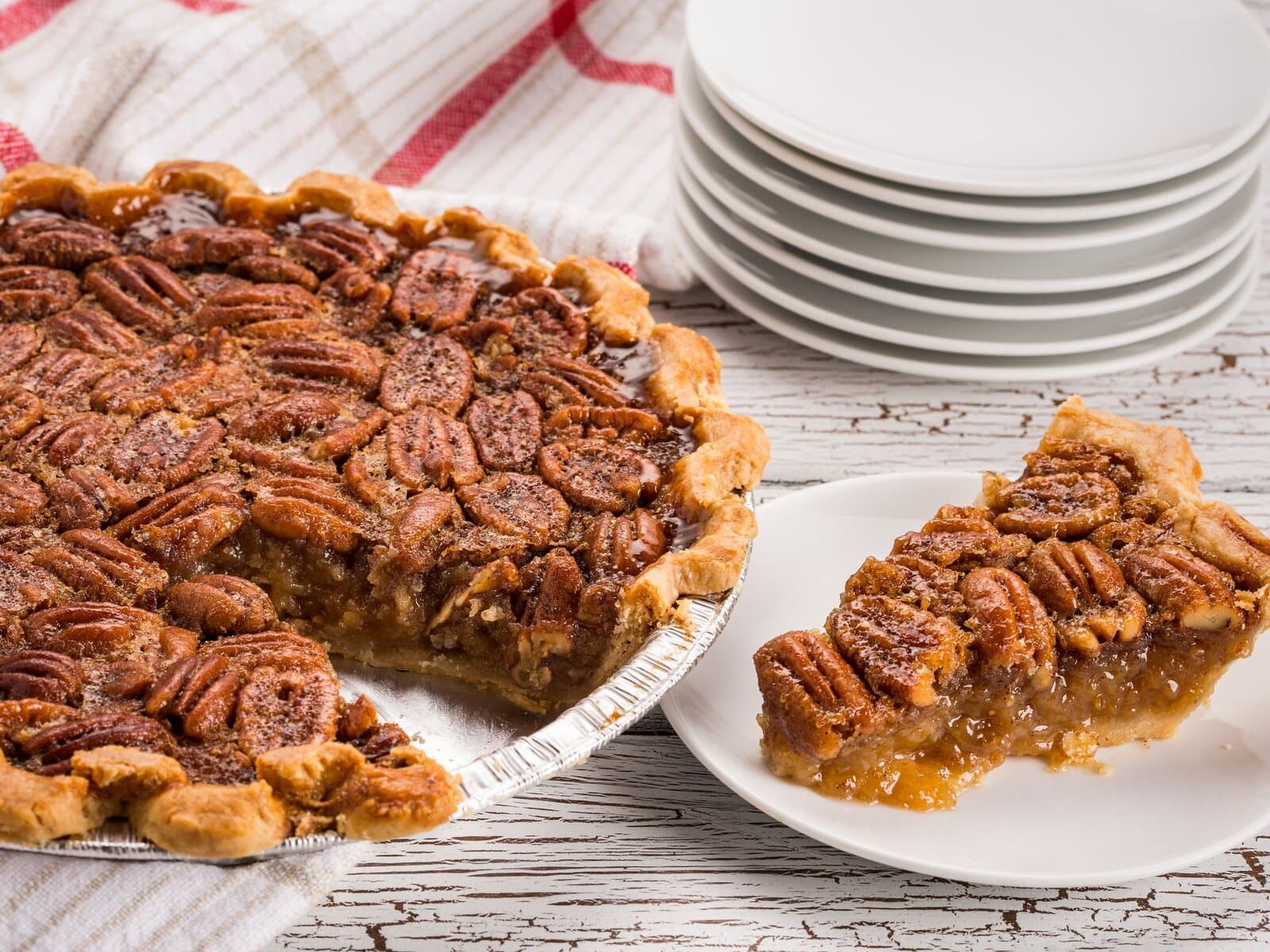 A whole pecan pie with toasted pecans and a slice served alongside.