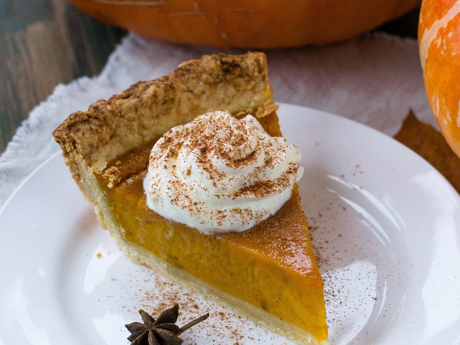 A slice of pumpkin pie with whipped cream on a white plate.